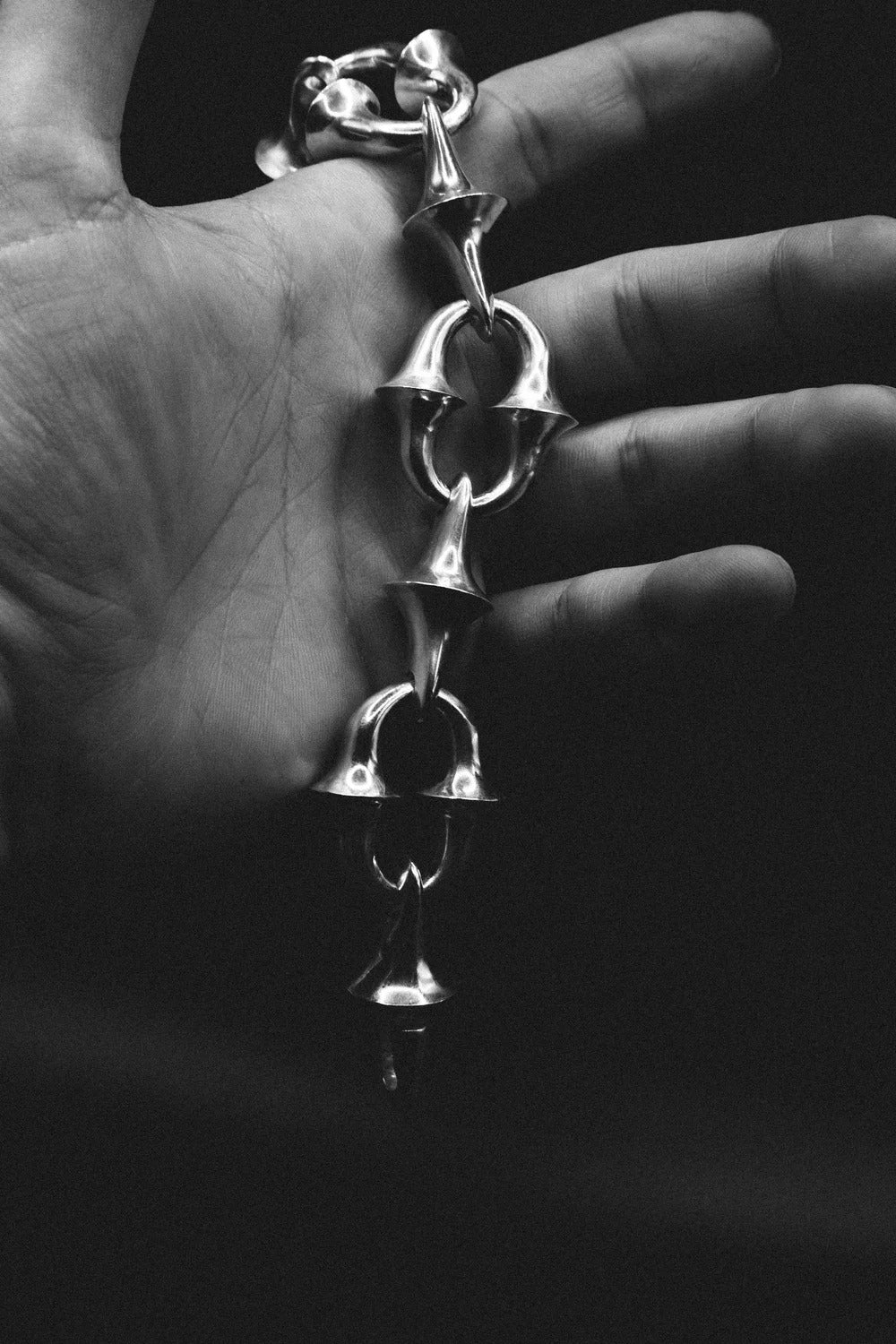Silver bracelet held in a hand against a dark background