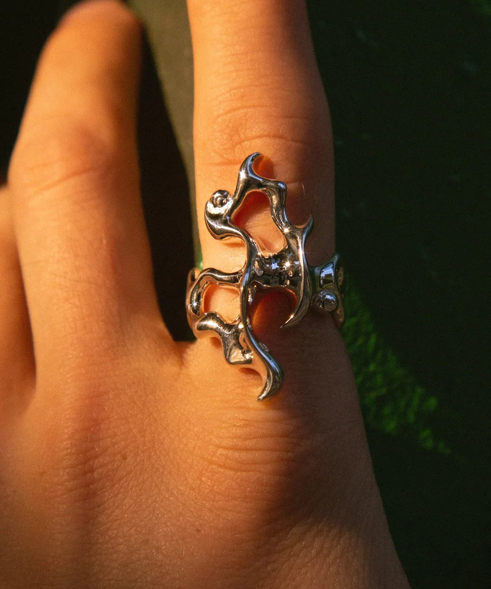 Silver ring with a unique design on a person's finger against a dark background