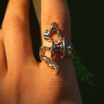 Silver ring with a unique design on a person's finger against a dark background